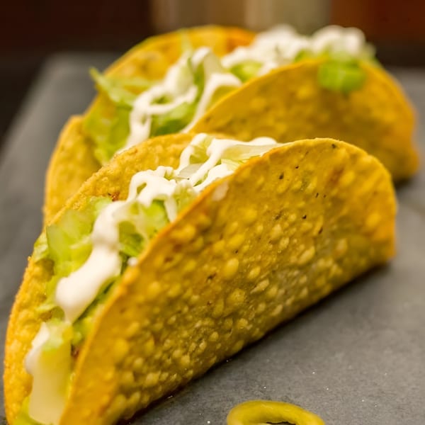 Three Fuego Mexican Kitchen hard-shell tacos filled with lettuce and drizzled with sour cream.