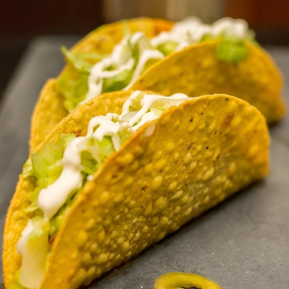 Three Fuego Mexican Kitchen hard-shell tacos filled with lettuce and drizzled with sour cream.