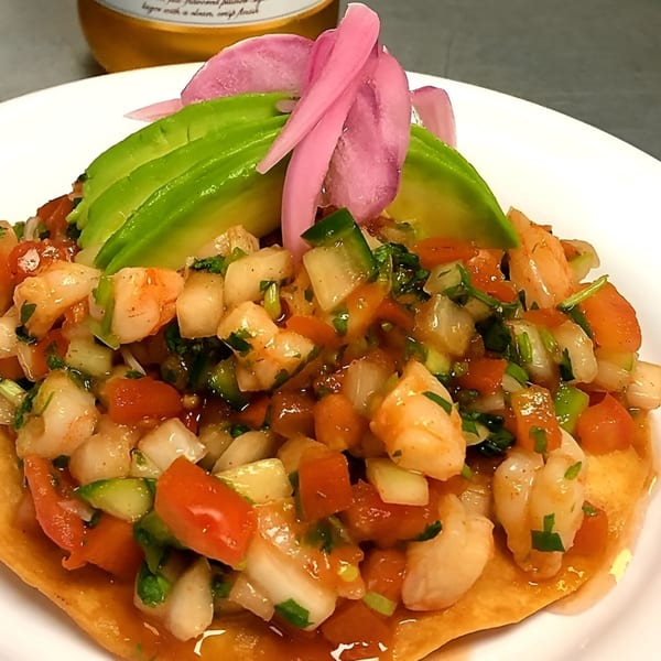 Shrimp ceviche tostada with diced tomatoes, onions, cilantro, avocado slices, and pickled red onions.