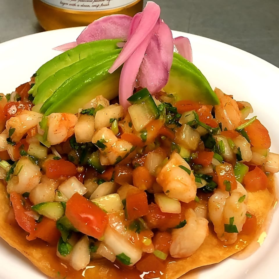 Shrimp ceviche tostada with diced tomatoes, onions, cilantro, avocado slices, and pickled red onions.